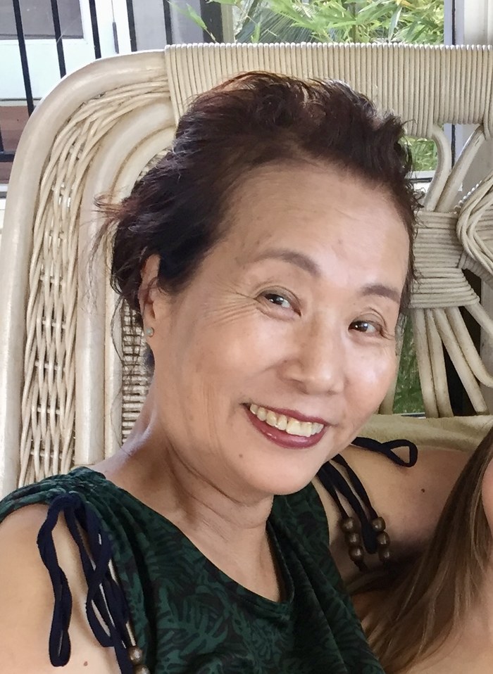 Michiko Okemoto, smiling, seated in a wicker chair.